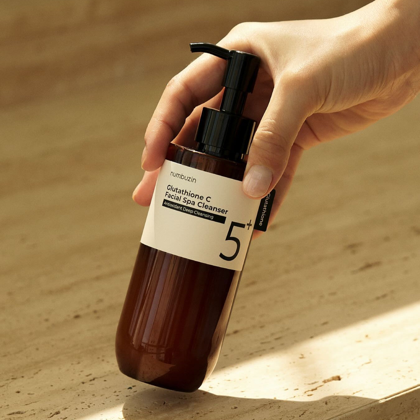 Hand holding NUMBUZIN No.5 Glutathione C Aroma Massage Deep Cleanser 200ml bottle on a beige background