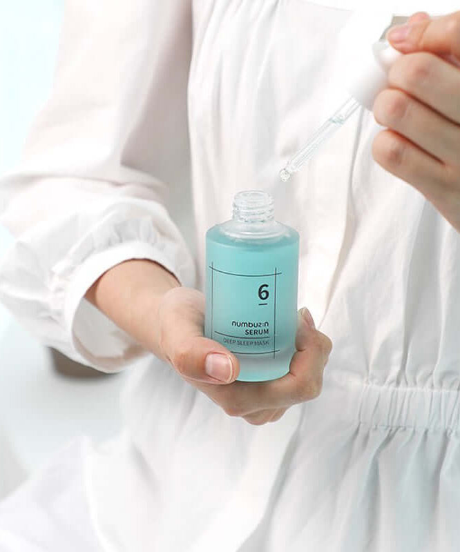 Close-up of a person holding NUMBUZIN No.6 Deep Sleep Mask Serum with dropper, white attire, enhancing night skincare routine.