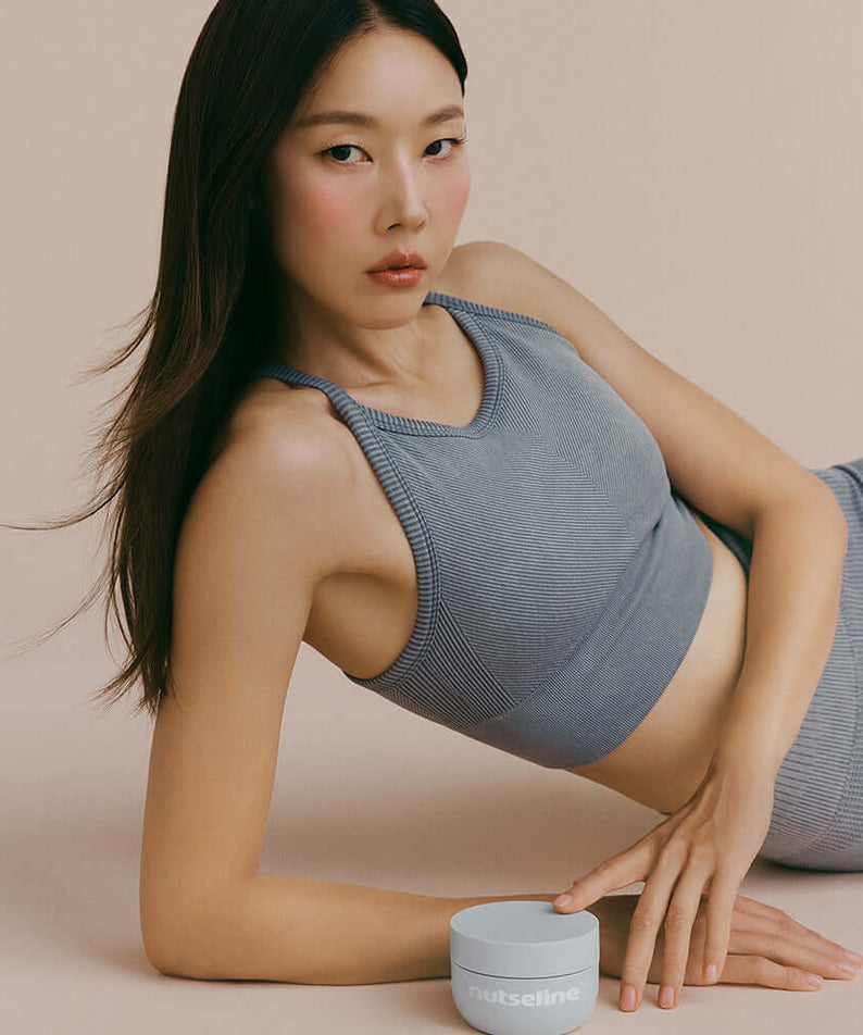 Woman posing with NUTSELINE Aroma Nut Gray Body Scrub 200g in a stylish setting.