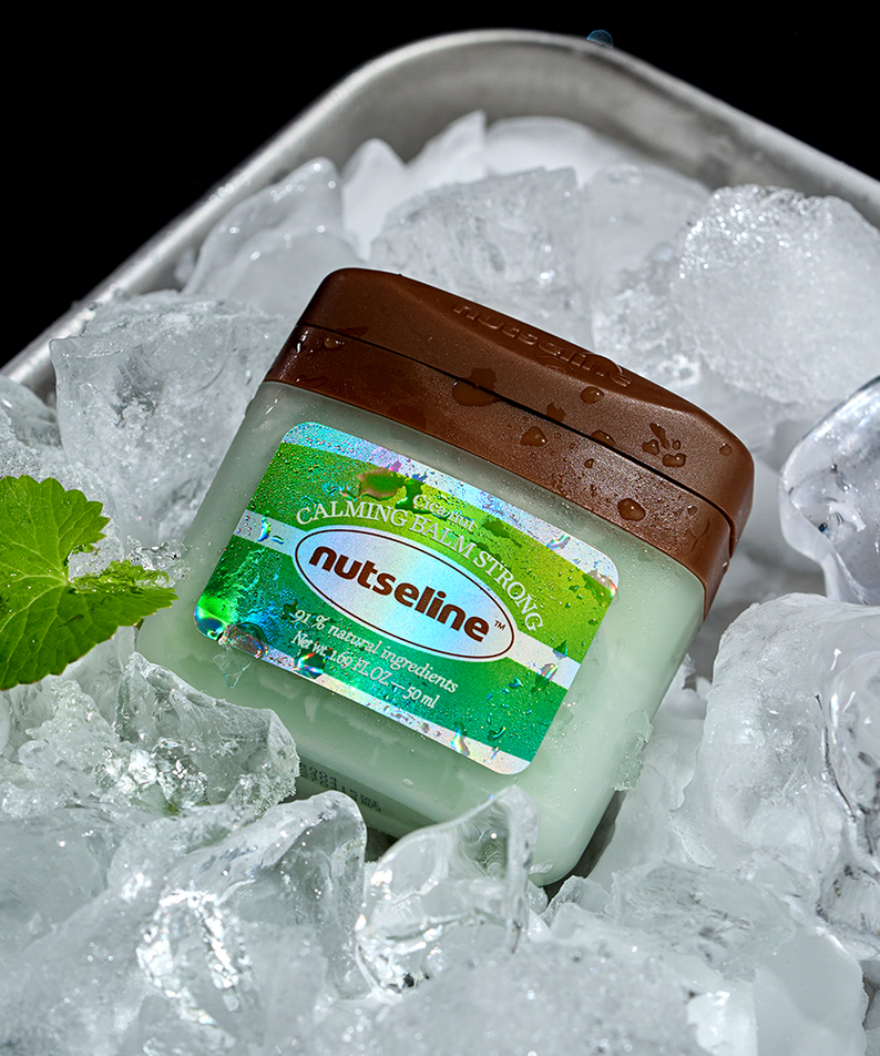 NUTSELINE Cica Nut Calming Balm Strong 50ml jar surrounded by ice and a green leaf, highlighting natural cooling ingredients.