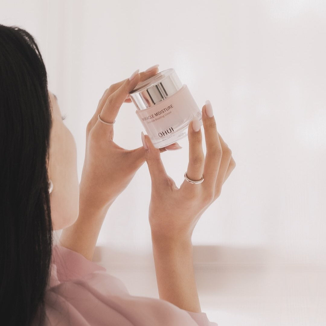 Woman holding OHUI Miracle Moisture Ceramide Boosting Cream 60ml in soft lighting
