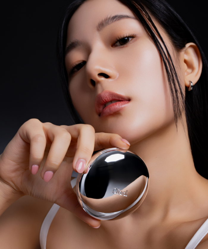 Woman holding OIAD Pore Perfecting Mirror Moon Cushion close to her face, showcasing skincare product's elegant design and functionality.
