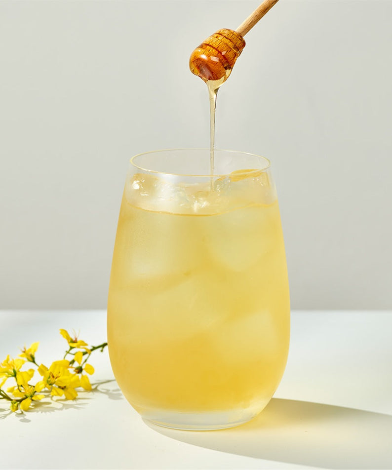 Glass of OSULLOC Canola & Apricot Tea 20 P with honey drizzling and canola flowers