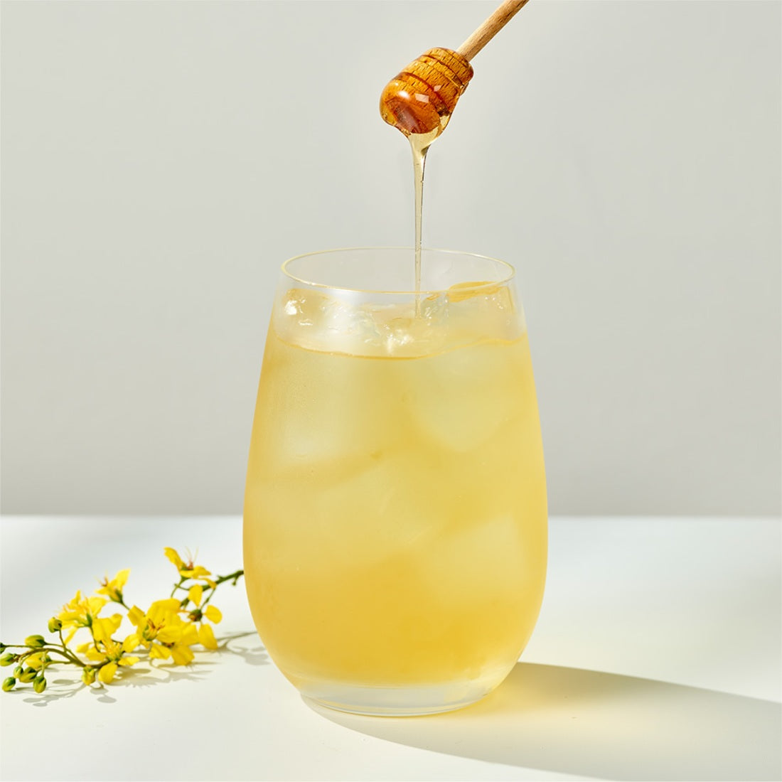 Glass of OSULLOC Canola & Apricot Tea 20 P with honey drizzling and canola flowers