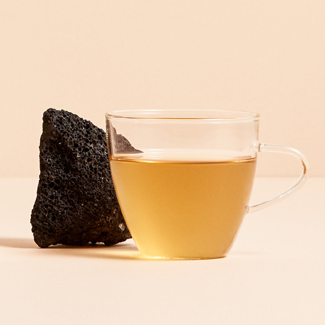 Glass cup of OSULLOC Jeju Volcanic Oolong Tea with volcanic rock behind on neutral background