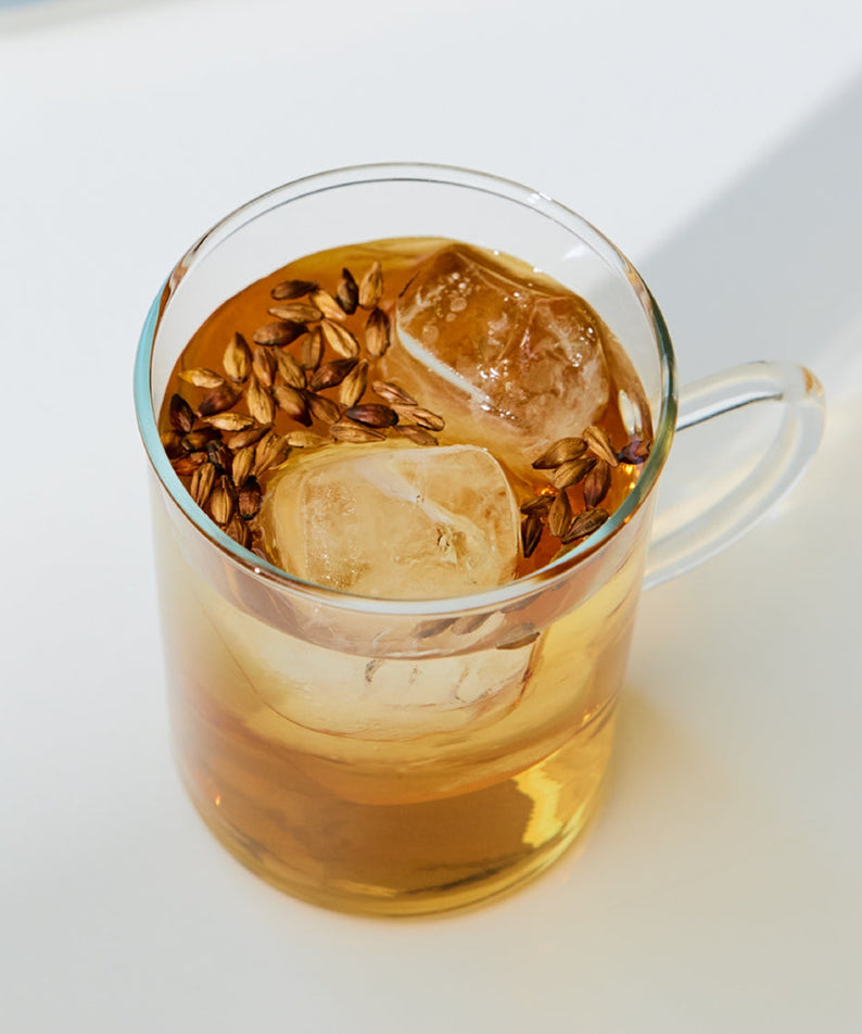 Glass cup of iced herbal tea with floating seeds on a white surface