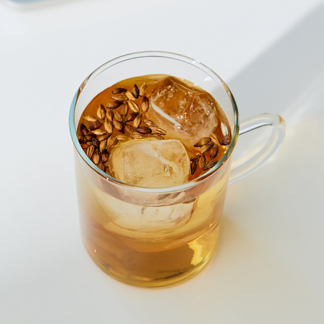 Glass cup of iced herbal tea with floating seeds on a white surface