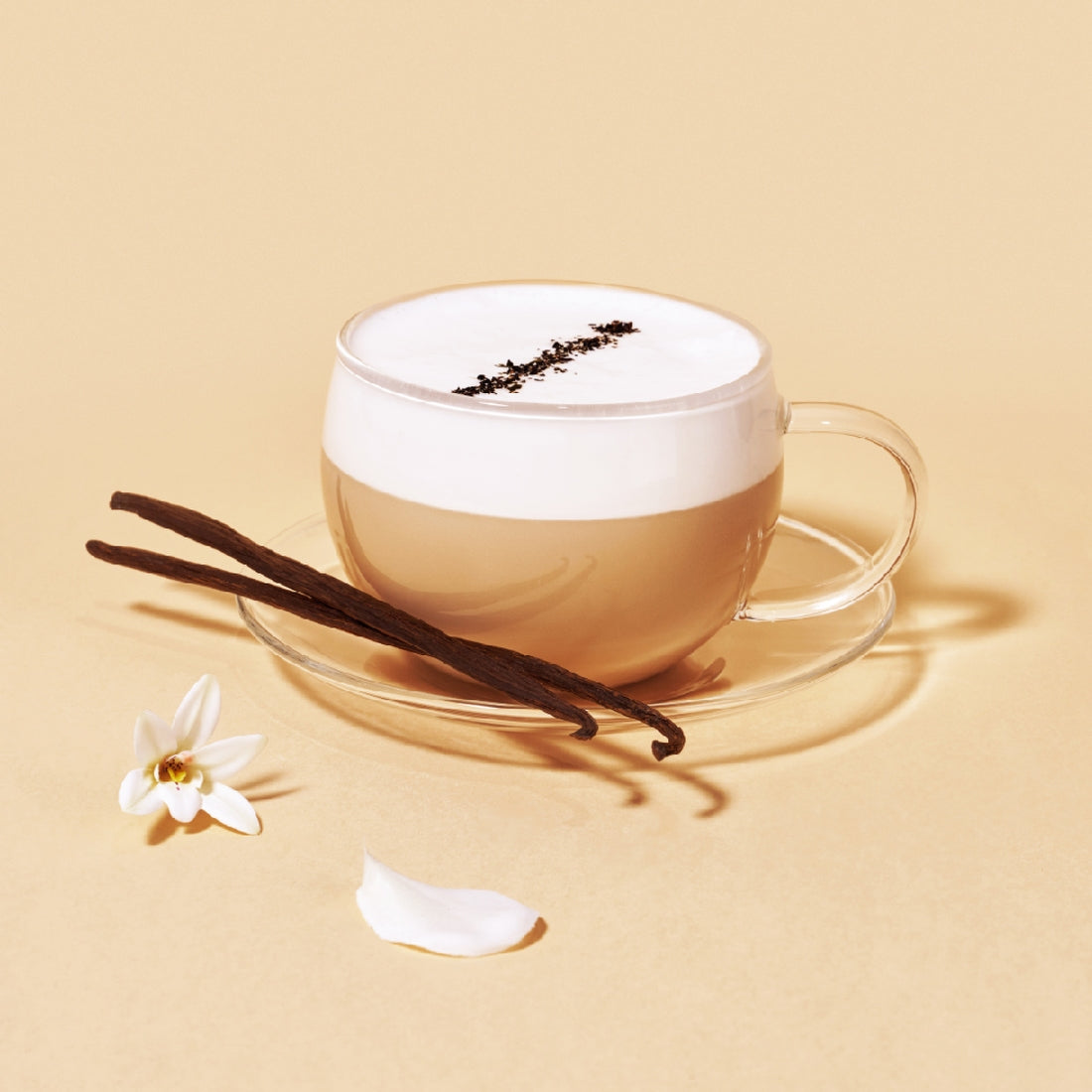 Glass cup of OSULLOC Vanilla Honey Black Tea with frothy cream, vanilla beans, and a delicate flower on a beige background.