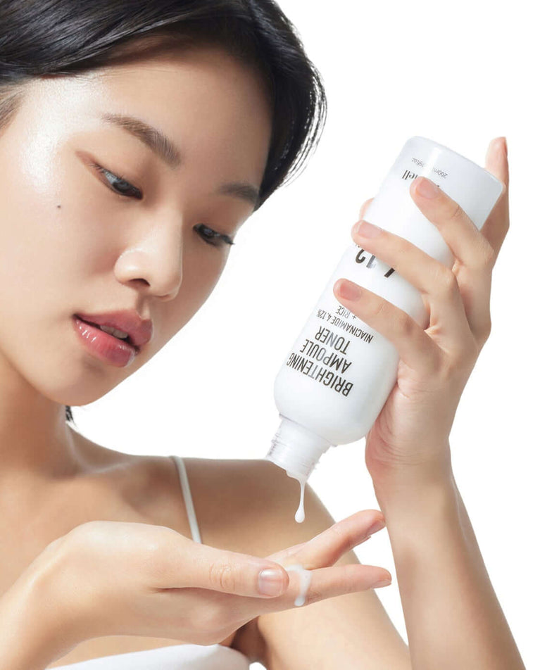 Woman applying PARNELL Niacinamide 4.12 Rice Brightening Ampoule Toner 200ml on her hand, demonstrating skincare routine.