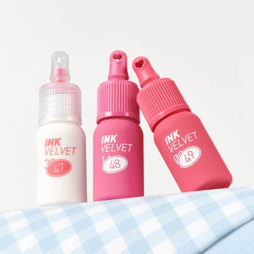 Three bottles of PERIPERA Ink The Velvet in pastel and pink shades displayed on a gingham fabric backdrop.