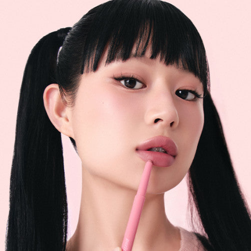 Model applying PERIPERA Puppy Plumping Dew Lip Pencil on lips with ponytail hairstyle, showcasing the product's color and texture.