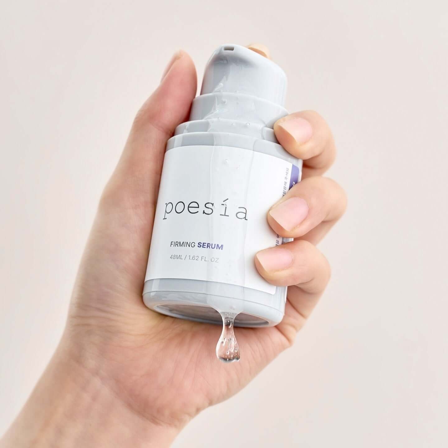 Hand holding POESÃA Hydro Phyto Collagen Deep Farming Ampoule Serum 48ml bottle with drop of serum.