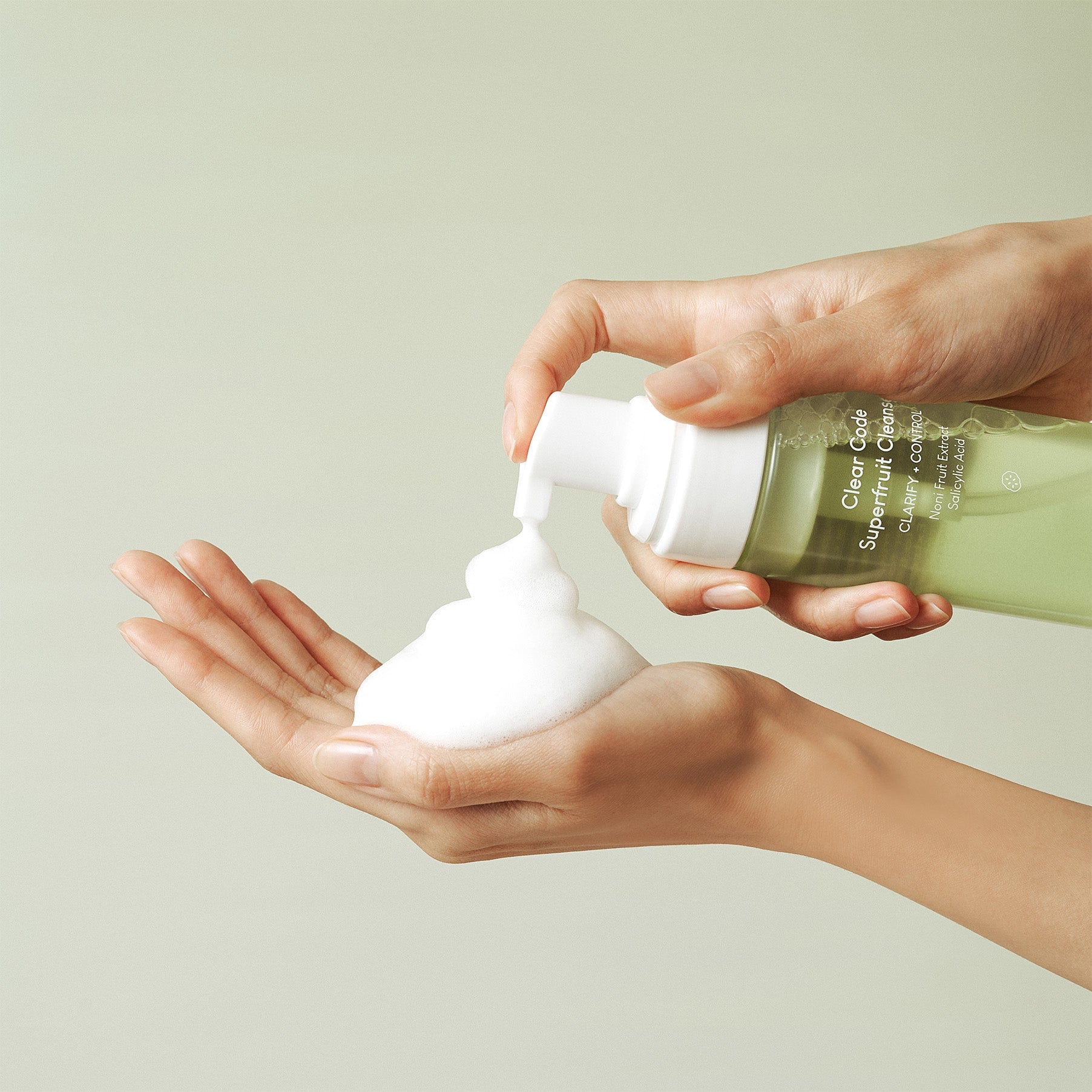 Hands using PURITO Clear Code Superfruit Cleanser 150ml, dispensing foamy cleanser into palm.