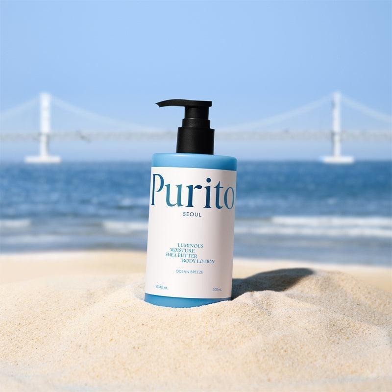 PURITO Luminous Moisture Shea Butter Body Lotion 300ml bottle on sand with a sea and bridge background
