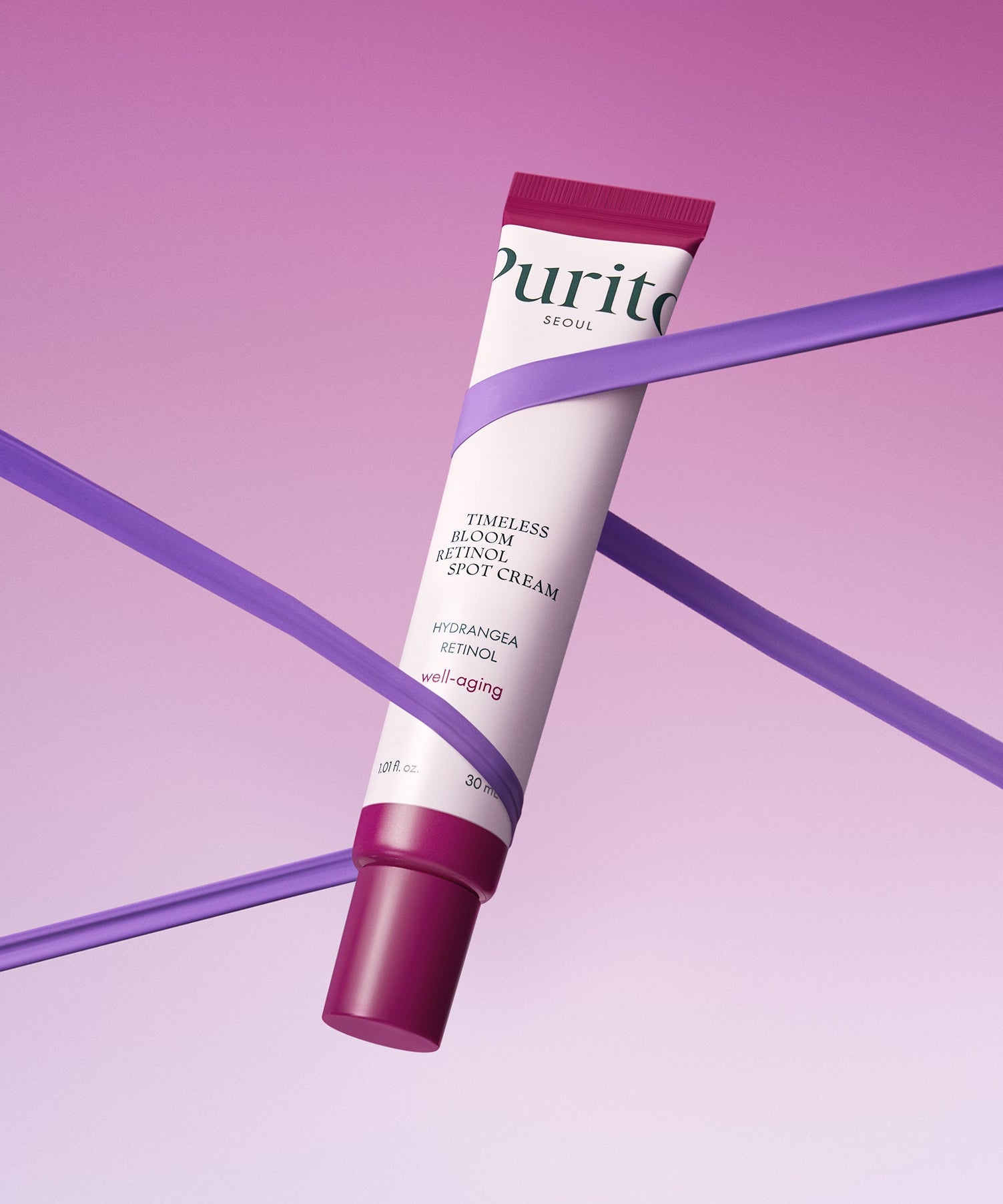 Purito Timeless Bloom Retinol Spot Cream 30ml against a pink background with purple ribbons.