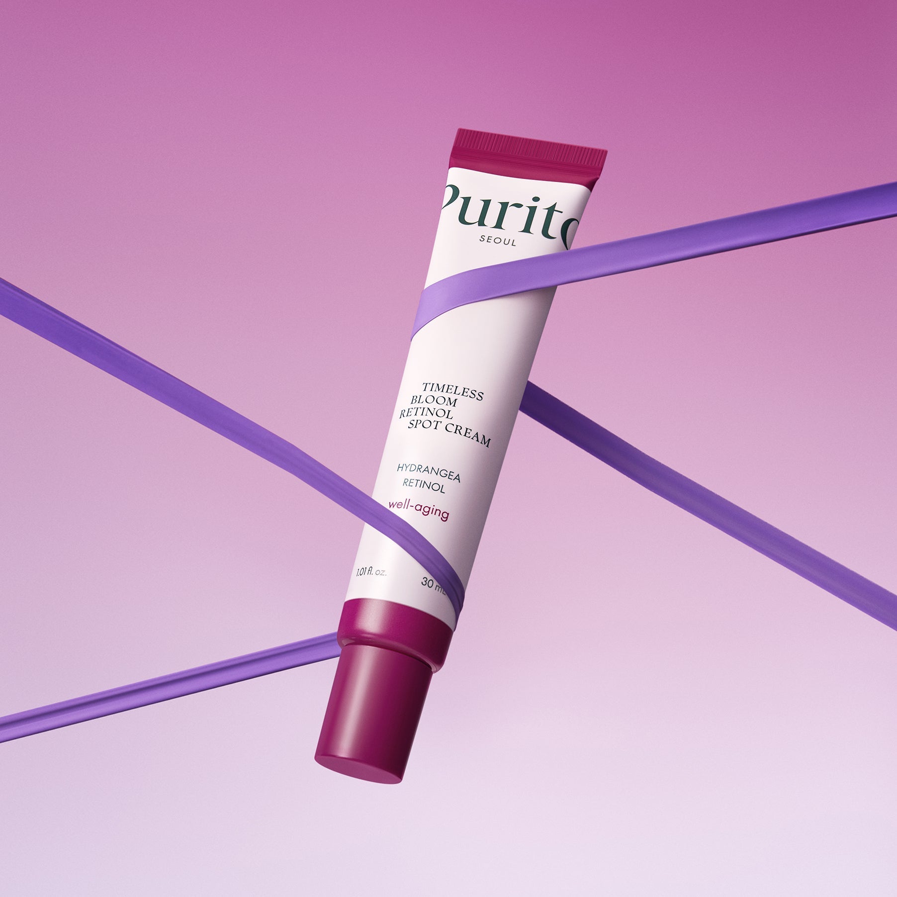 Purito Timeless Bloom Retinol Spot Cream 30ml against a pink background with purple ribbons.