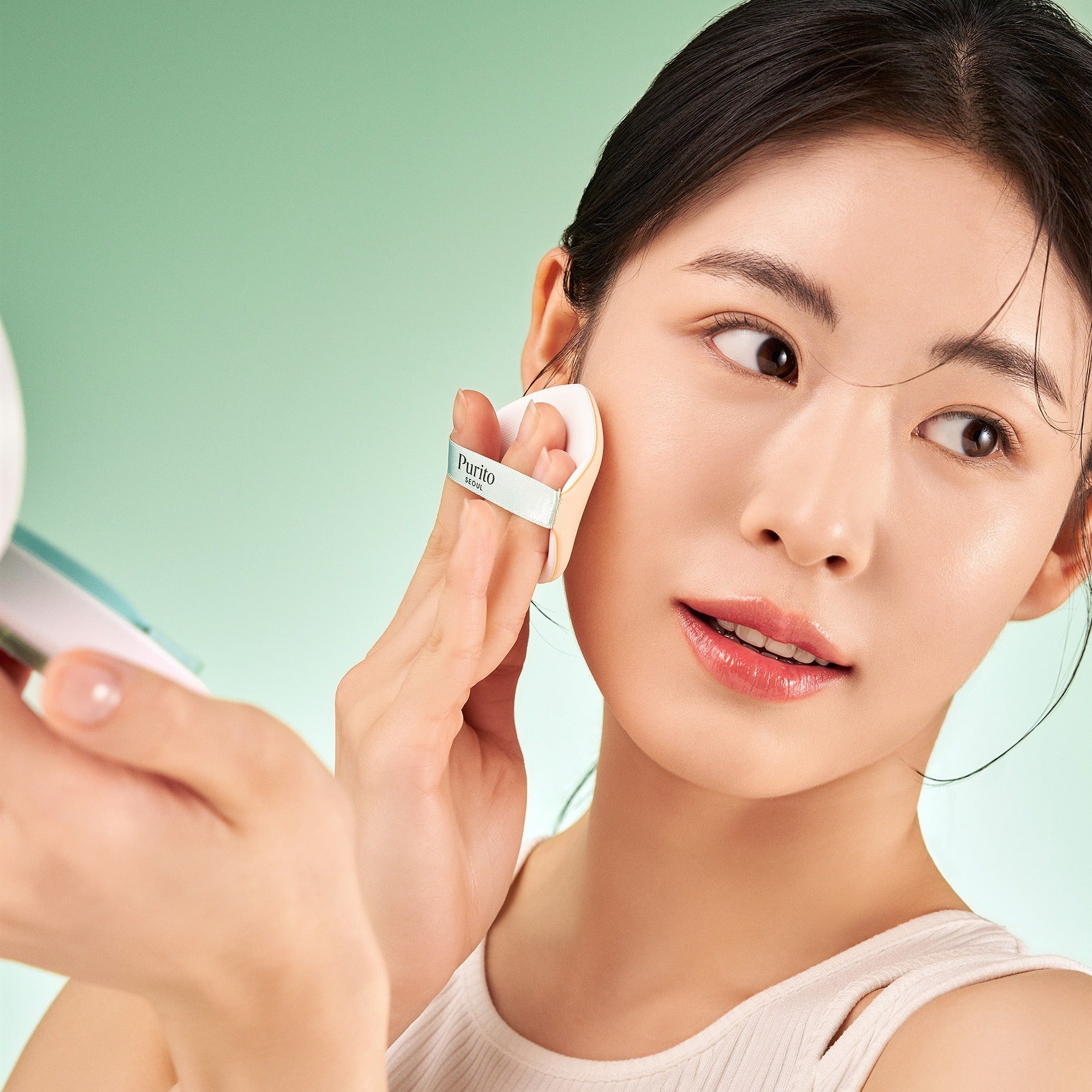 Person applying PURITO Wonder Relief Celtella BB Cushion 15g using compact mirror.