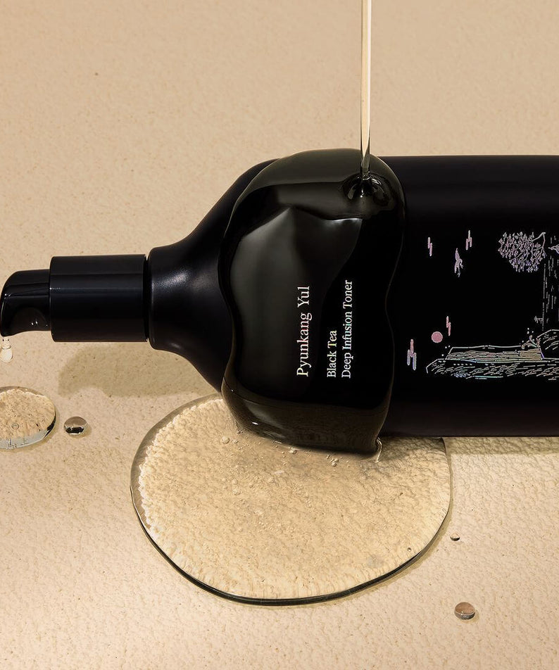 Bottle of PYUNKANG YUL Black Tea Deep Infushion Toner 130ml with spilling liquid, showcasing premium skincare product on beige background.