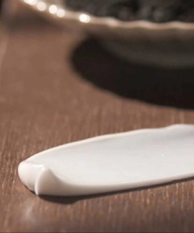 Texture of PYUNKANG YUL Black Tea Enriched Cream 60ml displayed on a wooden surface.