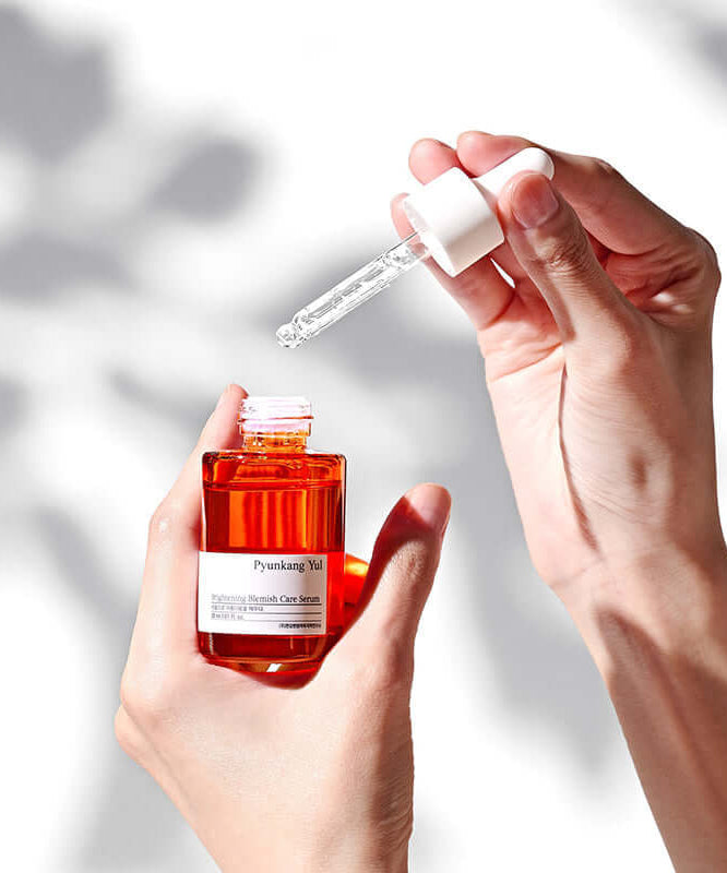 PYUNKANG YUL Brightening Blemish Care Serum 30ml in hands with dropper against light background