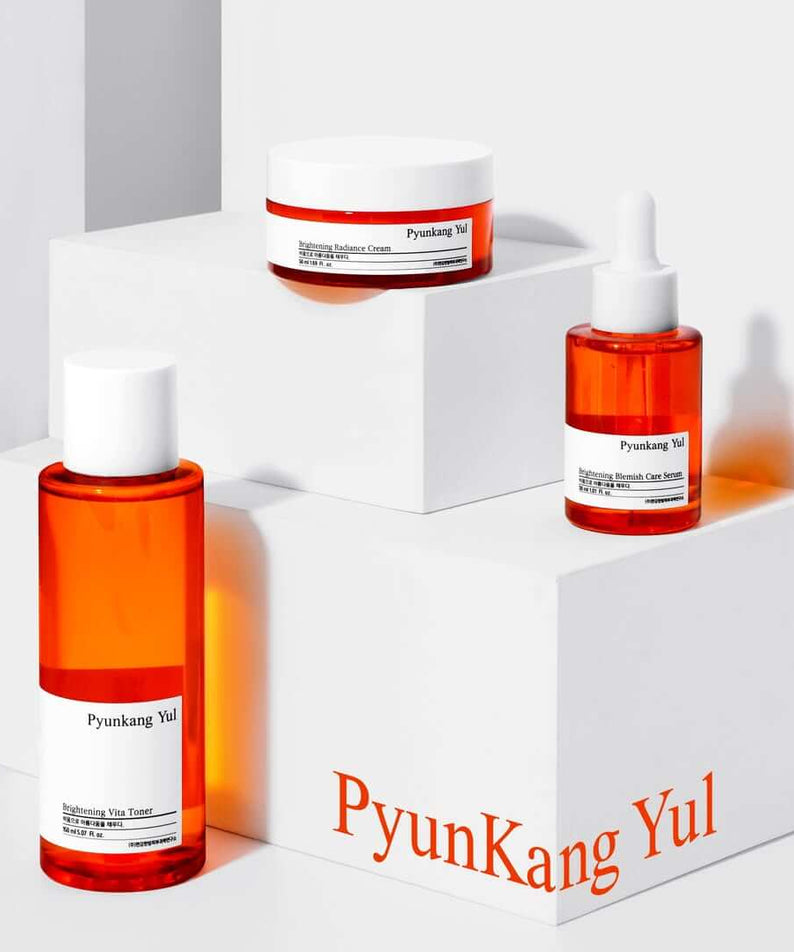 PYUNKANG YUL Brightening Bojagi Gift Set displayed on white blocks with toner, cream, and serum bottles.