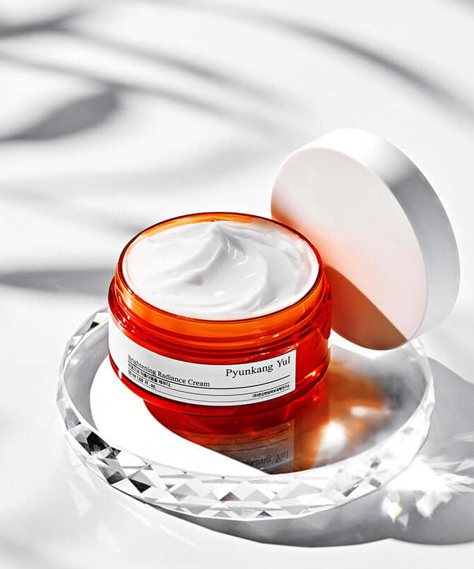 Open jar of PYUNKANG YUL Brightening Radiance Cream 50ml on a reflective surface