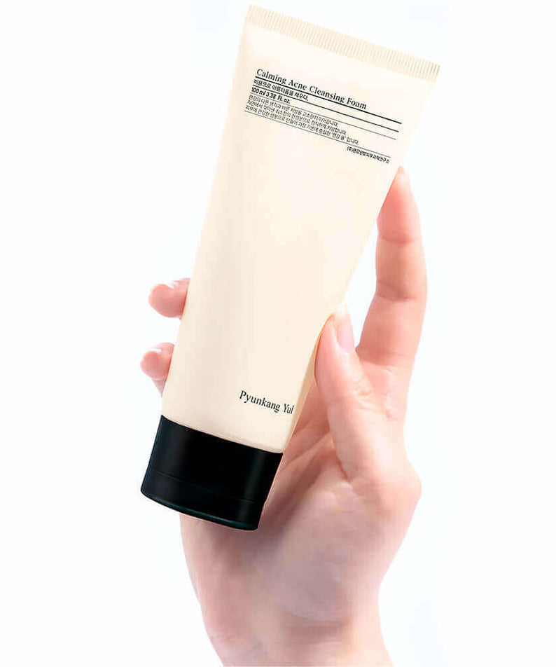 Hand holding PYUNKANG YUL Calming Acne Cleansing Foam 100ml tube on a white background.
