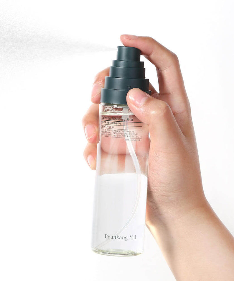 Hand holding PYUNKANG YUL Calming Moisture Mist 100ml spray bottle against white background, demonstrating product usage.