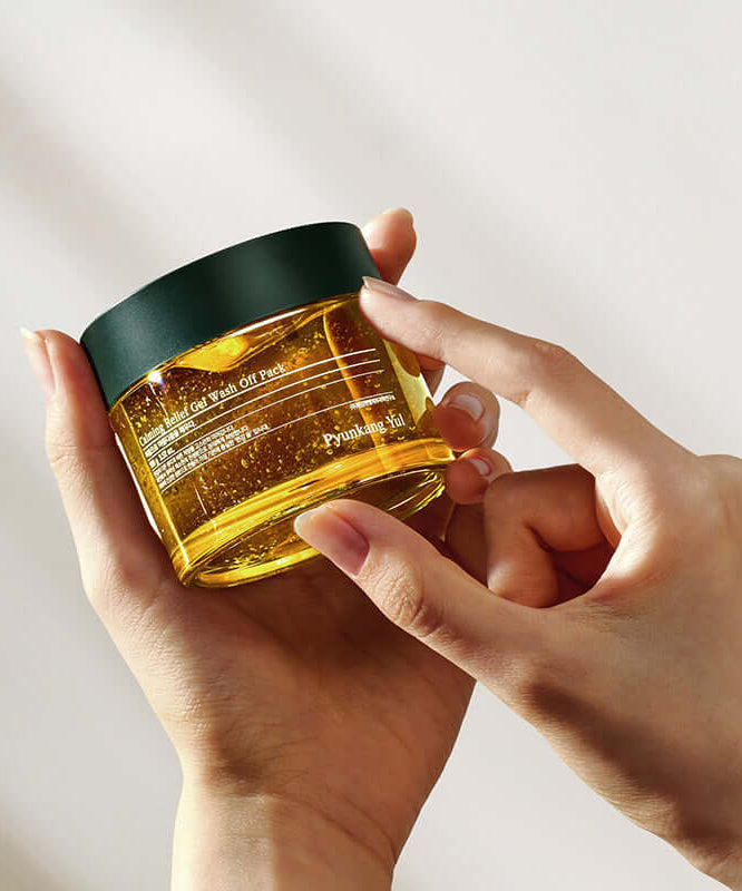 Hands holding PYUNKANG YUL Calming Relief Gel Wash-Off Pack 100g in a glass jar with green lid