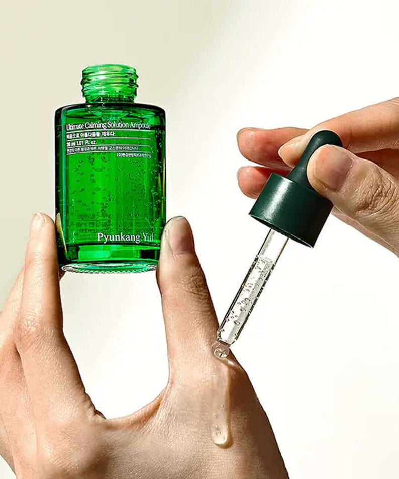 Hands pouring PYUNKANG YUL Ultimate Soothing Solution Ampoule 30ml from dropper bottle