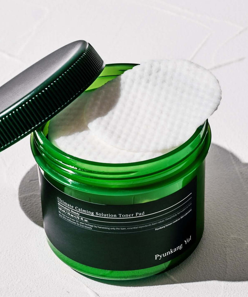 Open jar of PYUNKANG YUL Ultimate Soothing Solution Toner Pads 70 sheets 140ml with white pad halfway out on white background