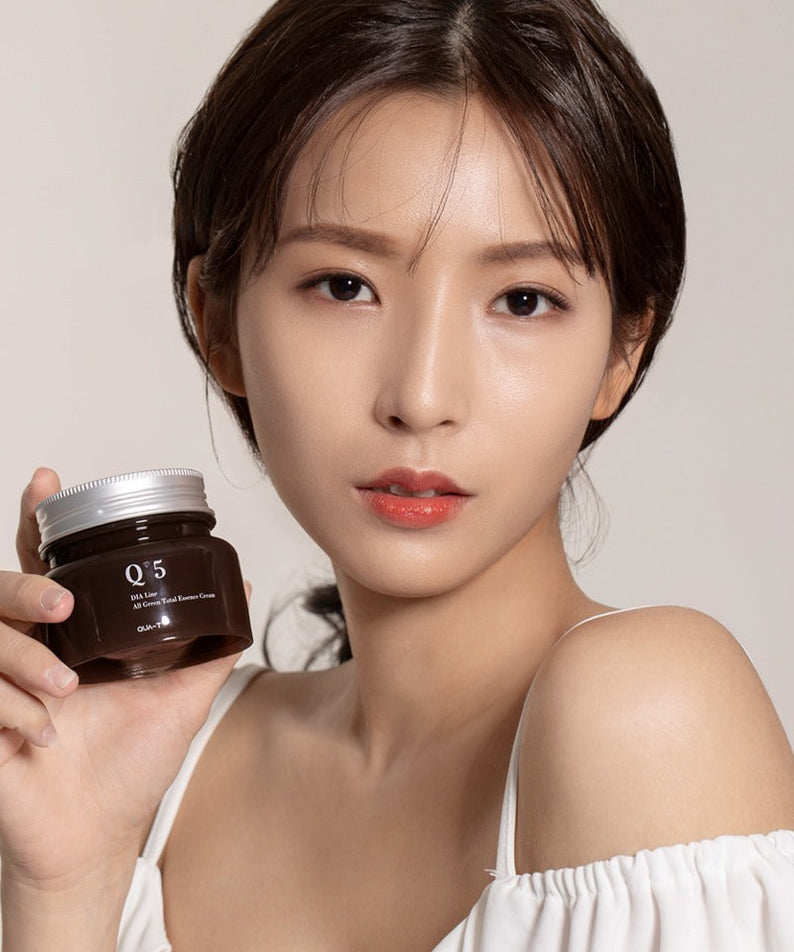 Person holding a jar of QUA-T Dia All Green Total Essence Cream 100ml, suitable for skincare routines.