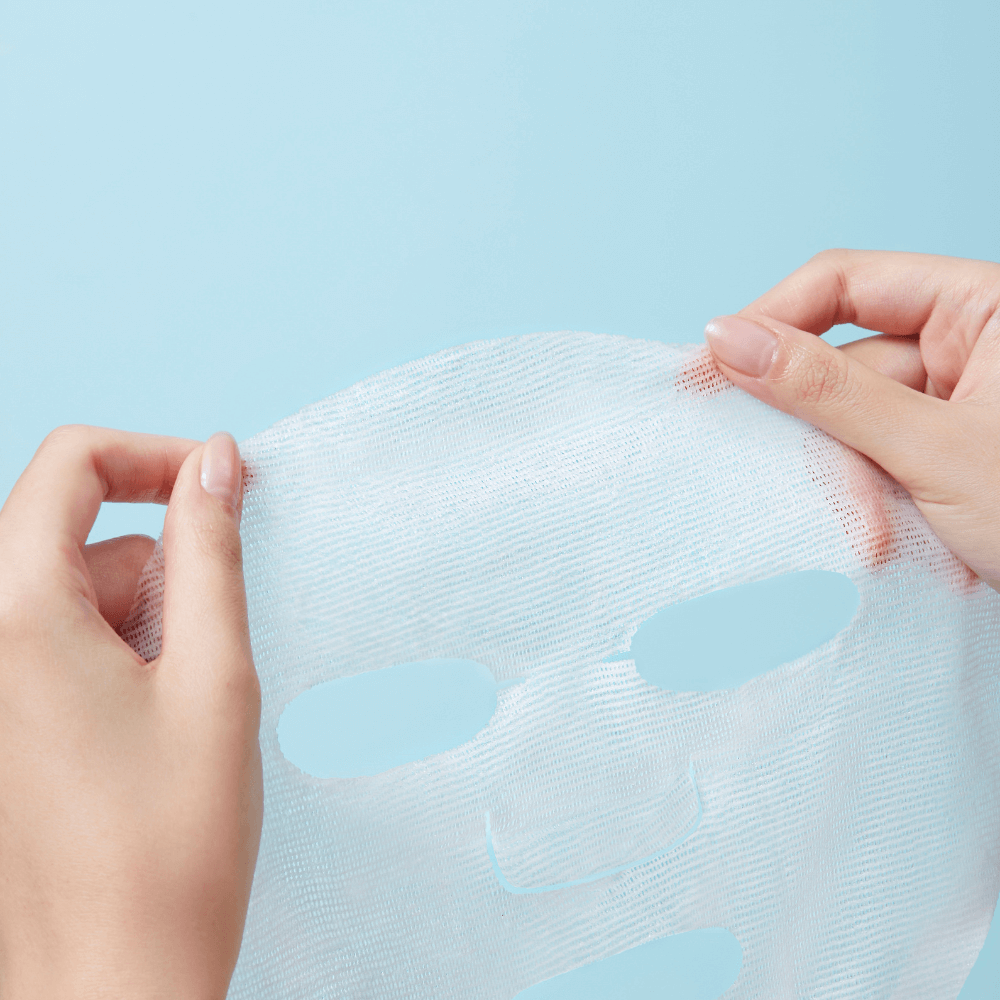 Person holding a REAL BARRIER Aqua Soothing Cream Mask sheet against a blue background.