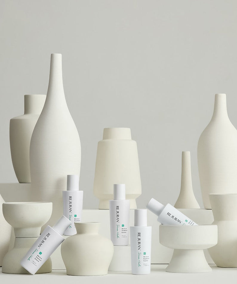 REJURAN Derma Healer Moisture Treatment Essence 70g displayed among artistic white vases.