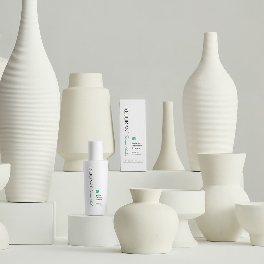 REJURAN Derma Healer Moisture Treatment Essence 70g bottle displayed among white ceramic vases.