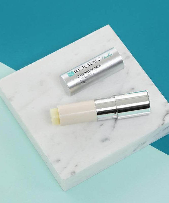 REJURAN Healer Calming Lip Balm 3.7g on marble surface with silver cap removed, showcasing minimalistic design and soothing product features