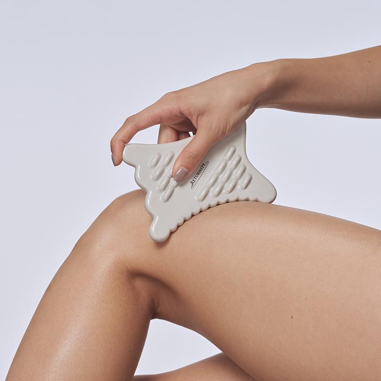 Person using RETURNITY Guasha tool on leg for massage