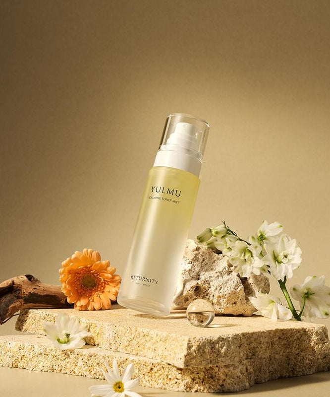 RETURNITY Yulmu Calming Toner Mist 100ml bottle surrounded by flowers on a textured stone surface.