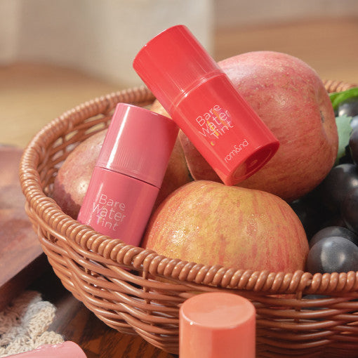 ROMAND Bare Water Tint in a basket with apples and grapes, showcasing vibrant lip color options.