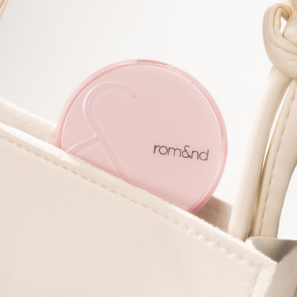ROMAND Bloom in Coverfit Cushion mini in a light pink compact, placed inside a beige bag, showcasing its travel-friendly design.