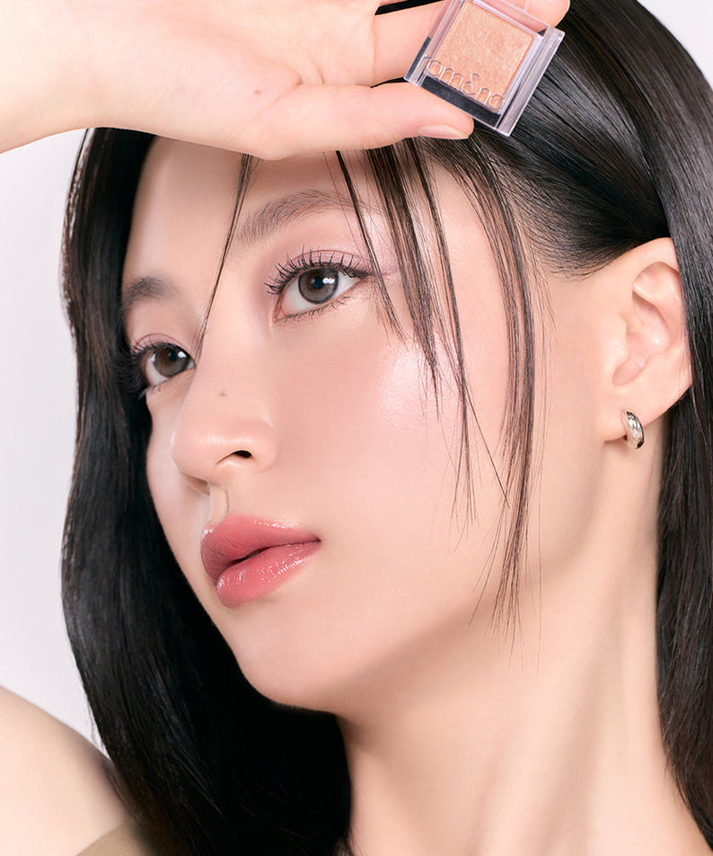 Person holding ROMAND Slide In Single makeup product near their face, showcasing vibrant cosmetic color on smooth skin.