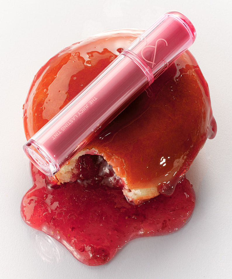 ROMAND The Juicy Lasting Tint in vibrant pink shade placed on glossy red surface, showcasing its rich and long-lasting color.