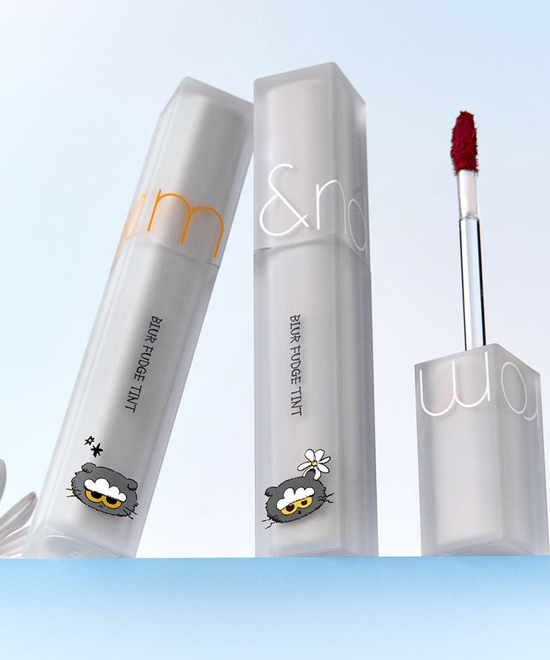 ROMAND x Joanne Friends Blur Fudge Tint makeup product with decorative packaging and lip tint applicator on a light background.