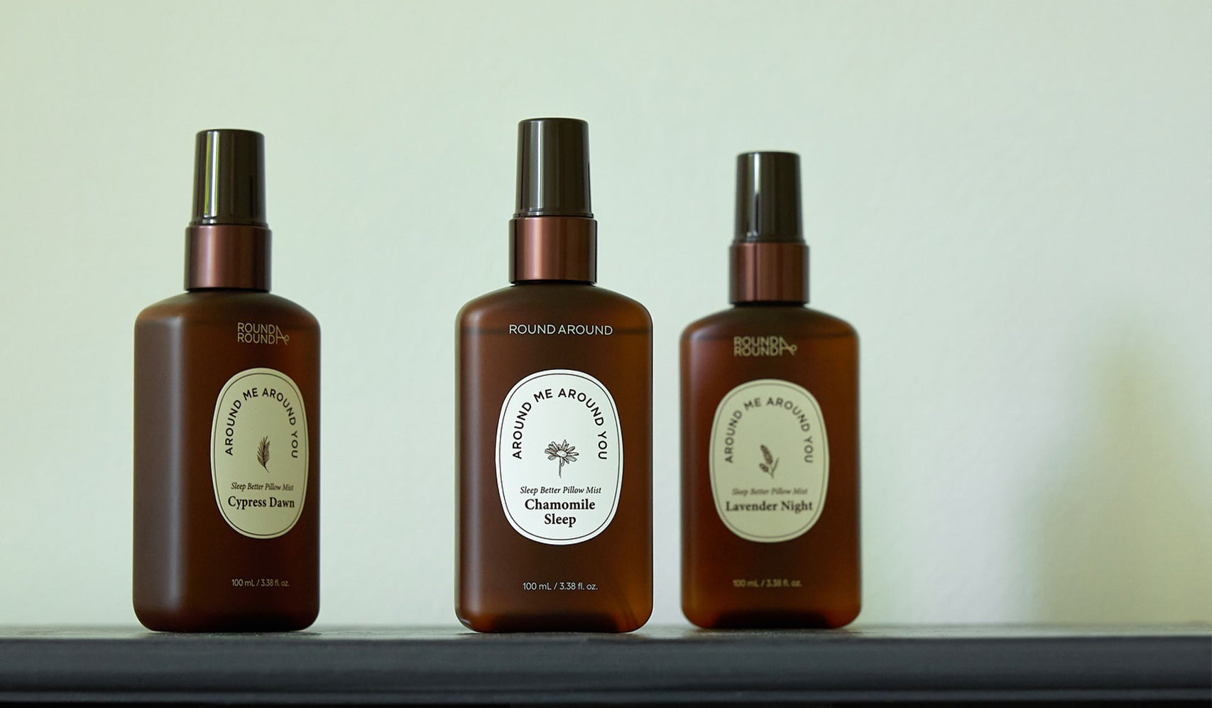 Three aromatherapy spray bottles labeled Cypress Dew, Chamomile Sleep, and Lavender Night on a shelf against a plain background.