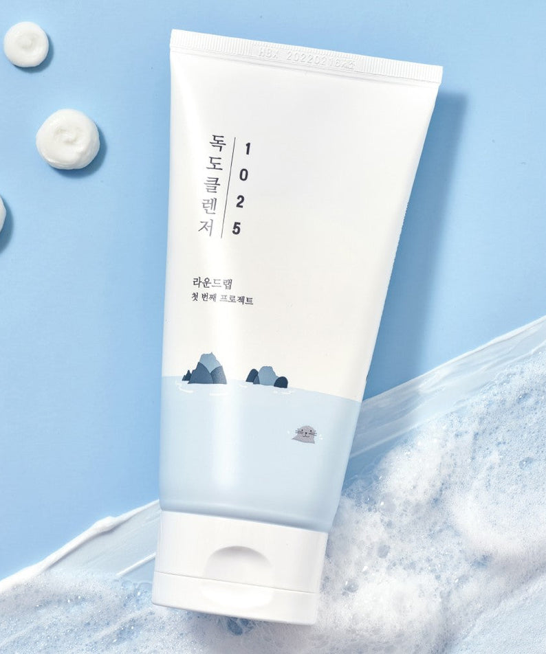 ROUND LAB 1025 Dokdo Cleanser 150ml tube on a textured background with foam spots.