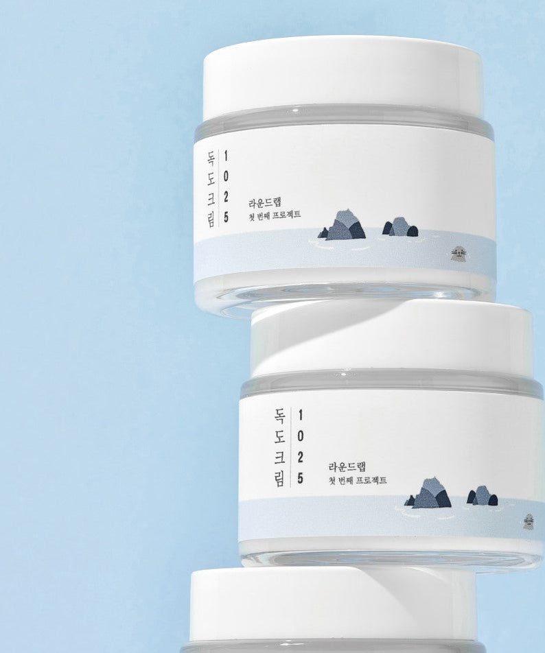 Image of ROUND LAB 1025 Dokdo Cream 80ml stacked jars with minimalist design on blue background