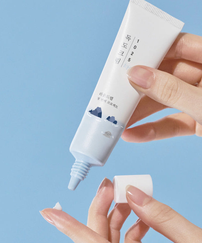 Person applying ROUND LAB 1025 Dokdo Eye Cream 30ml on finger from tube against blue background