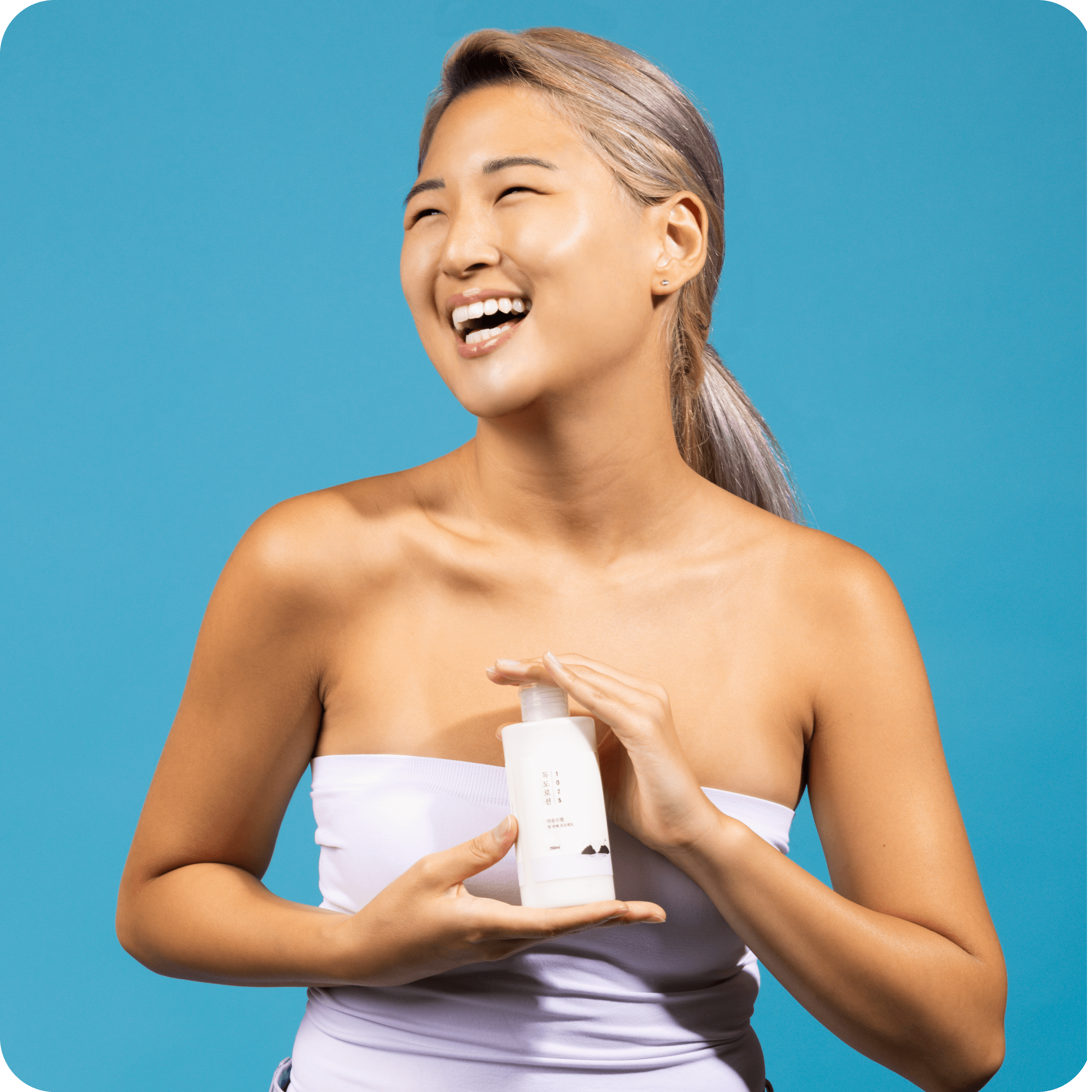 Smiling person holding ROUND LAB 1025 Dokdo Lotion 400ml against a blue background