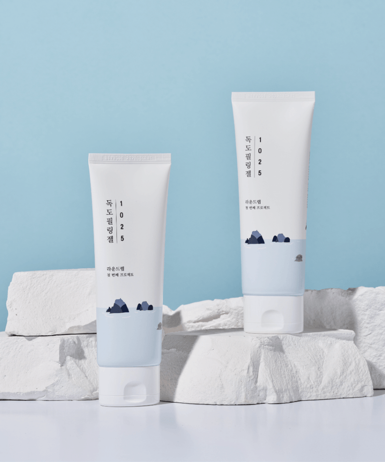 Two tubes of ROUND LAB 1025 Dokdo Peeling Gel 120ml placed on white rocks against a blue background for skincare routine.