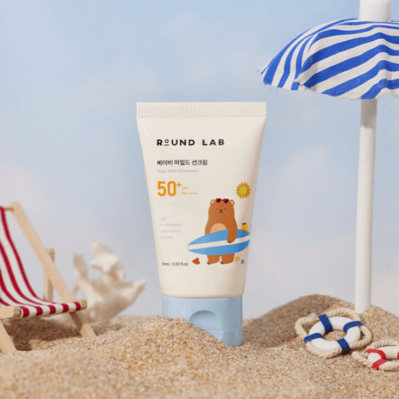 ROUND LAB Baby Mild Sun Cream 60ml on a beach with umbrellas and sand, SPF 50+ product in a playful design, 60ml bottle